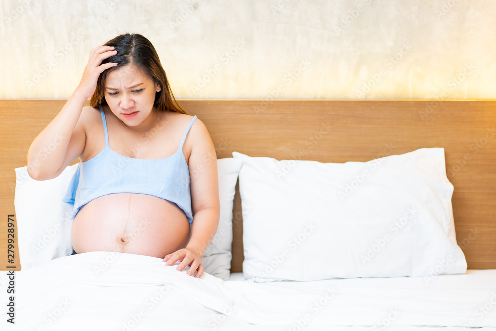 Asian pregnant woman sitting on the bed in unhappy emotion. Asian pregnant woman sitting on the bed in unhappy emotion.
