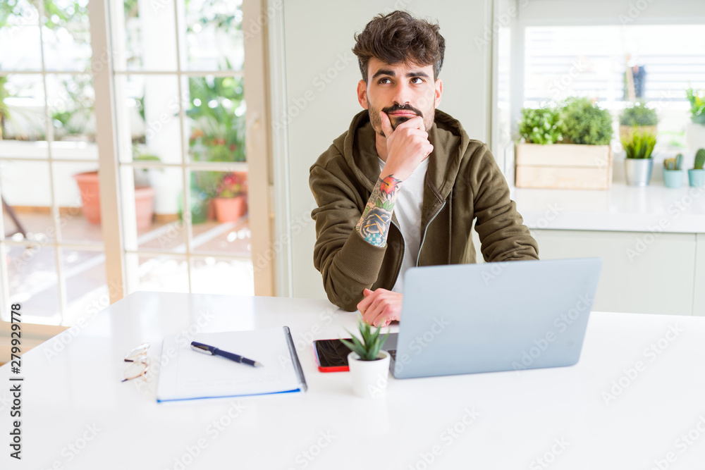 Young student man using computer laptop and notebook serious face thinking about question, very confused idea Young student man using computer laptop and notebook serious face thinking about question, very confused idea
