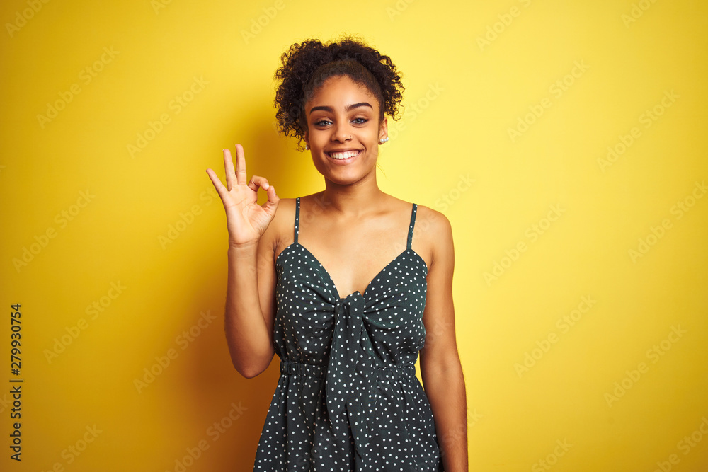 African american woman wearing summer casual green dress over isolated yellow background smiling positive doing ok sign with hand and fingers. Successful expression.