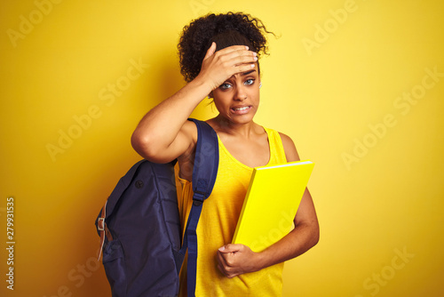 American student woman wearing backpack holding notebook over isolated yellow background stressed with hand on head, shocked with shame and surprise face, angry and frustrated. Fear and upset 