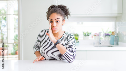 Beautiful african american woman with afro hair wearing casual striped sweater hand on mouth telling secret rumor  whispering malicious talk conversation