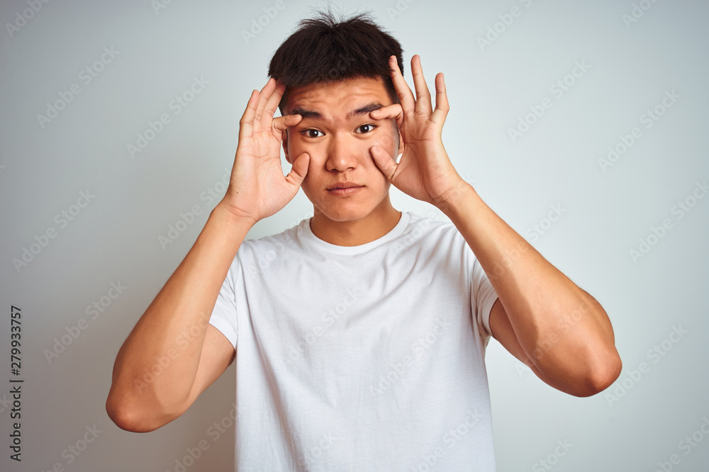 Young asian chinese man wearing t-shirt standing over isolated white background Trying to open eyes with fingers, sleepy and tired for morning fatigue Young asian chinese man wearing t-shirt standing over isolated white background Trying to open eyes with fingers, sleepy and tired for morning fatigue