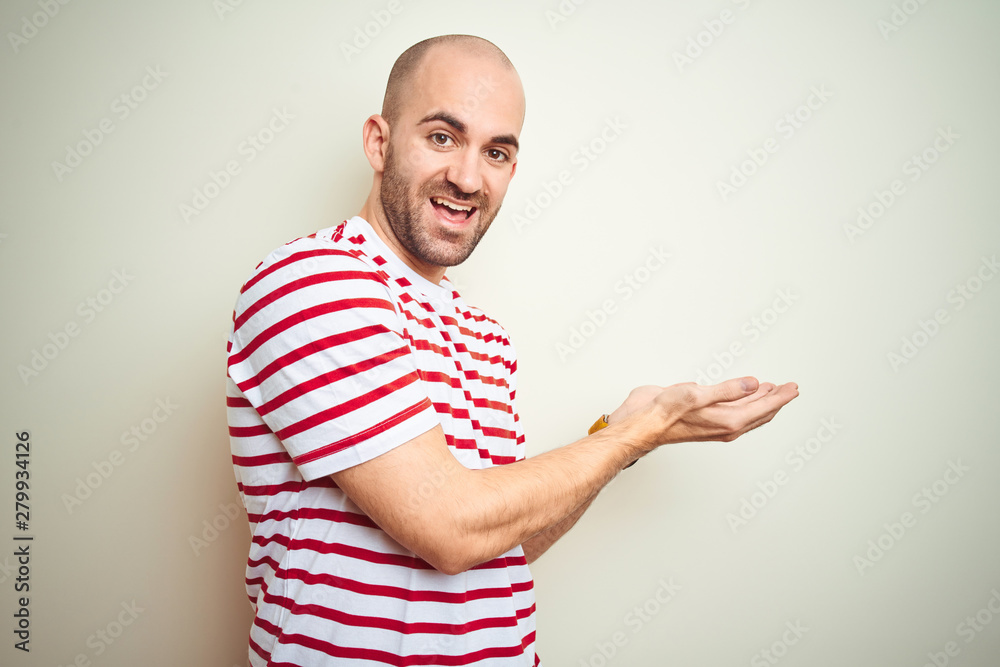 Naklejka premium Young bald man with beard wearing casual striped red t-shirt over white isolated background pointing aside with hands open palms showing copy space, presenting advertisement smiling excited happy