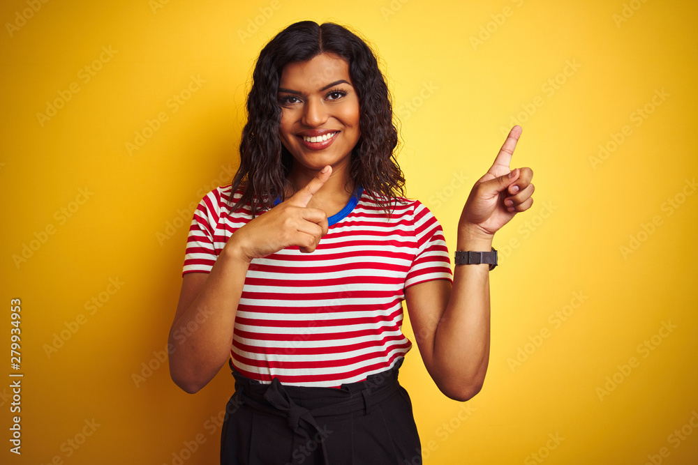 Transsexual transgender woman wearing stiped t-shirt over isolated yellow background smiling and looking at the camera pointing with two hands and fingers to the side. Transsexual transgender woman wearing stiped t-shirt over isolated yellow background smiling and looking at the camera pointing with two hands and fingers to the side.