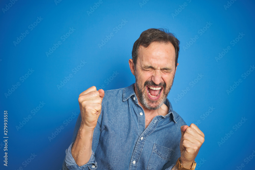 Handsome middle age senior man with grey hair over isolated blue background very happy and excited doing winner gesture with arms raised, smiling and screaming for success. Celebration concept. Handsome middle age senior man with grey hair over isolated blue background very happy and excited doing winner gesture with arms raised, smiling and screaming for success. Celebration concept.