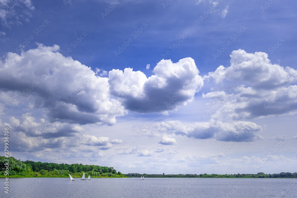 Sailboats sailing on a river under beautiful sky with white fluffy clouds