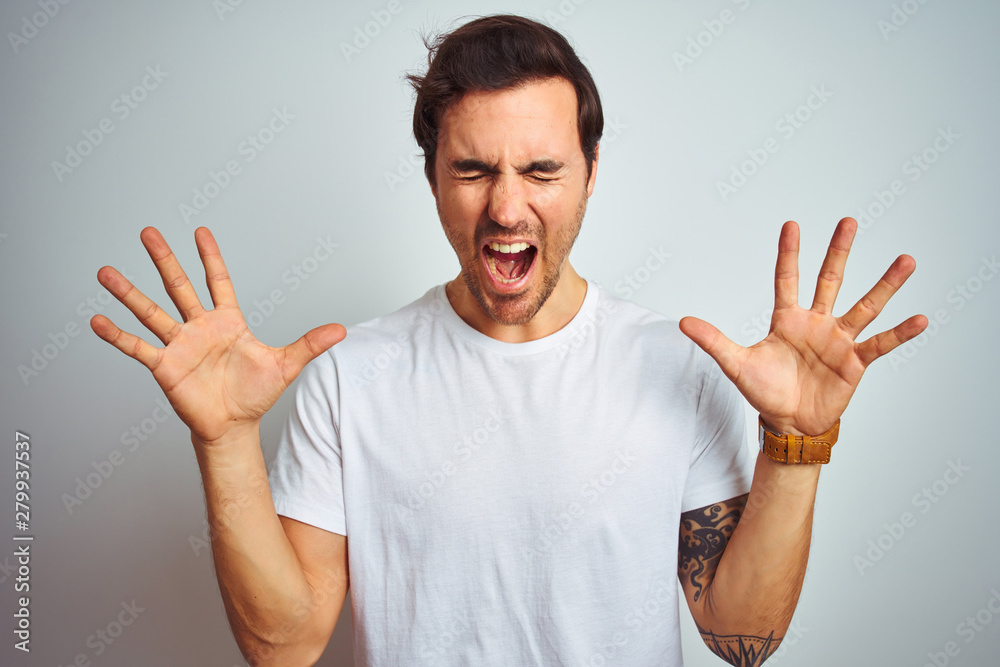 Young handsome man with tattoo wearing casual t-shirt over isolated white background celebrating mad and crazy for success with arms raised and closed eyes screaming excited. Winner concept