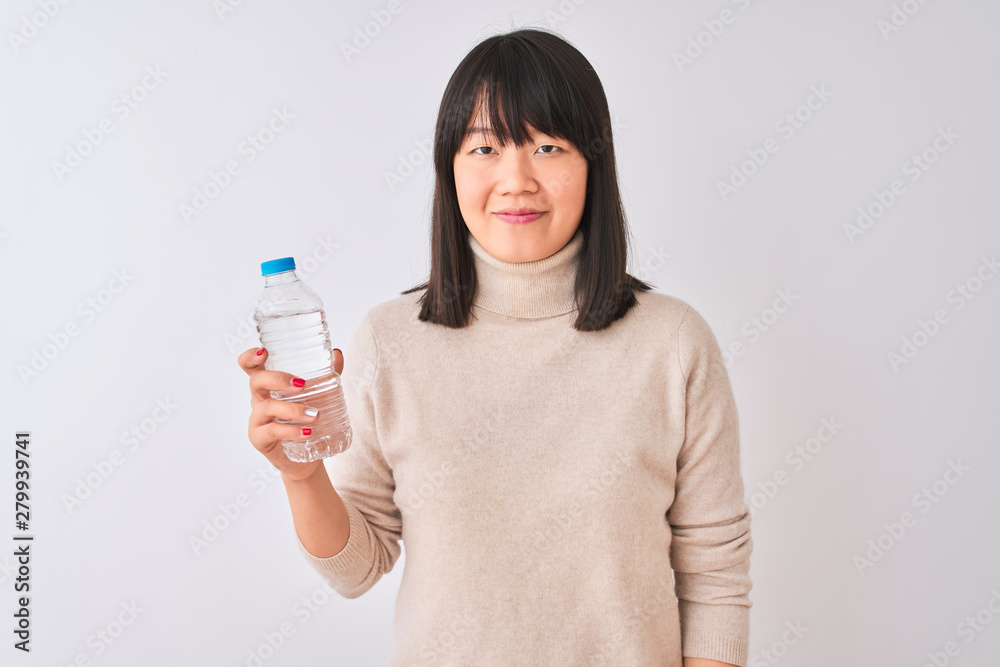 Young beautiful Chinese woman holding bottle of water over isolated white background with a confident expression on smart face thinking serious Young beautiful Chinese woman holding bottle of water over isolated white background with a confident expression on smart face thinking serious