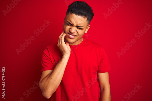 Young brazilian man wearing t-shirt standing over isolated red background touching mouth with hand with painful expression because of toothache or dental illness on teeth. Dentist concept. © Krakenimages.com