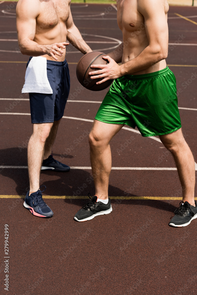 partial view of two shirtless sportsmen playing basketball at basketball court in sunny day