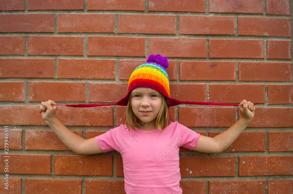 girl in rainbow knitted hat on a brick background.