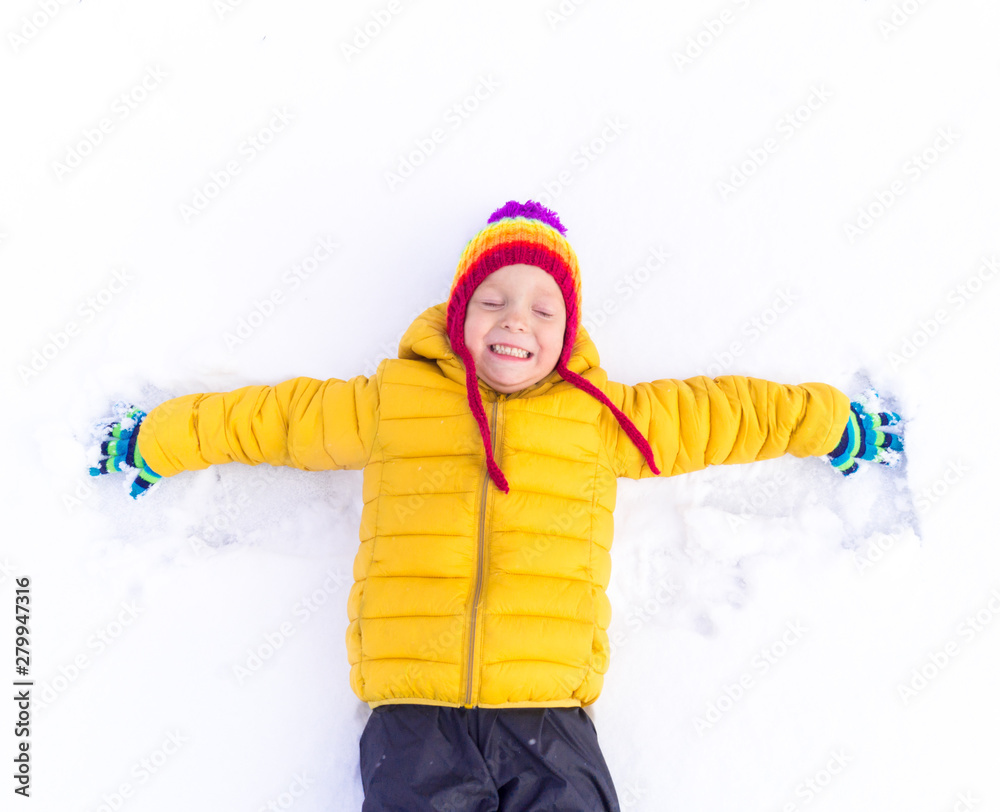 Kid in the yellow jacket is lying on the white snow Kid in the yellow jacket is lying on the white snow