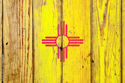 New Mexico US state national flag on a gray wooden boards background on the day of independence in different colors of blue red and yellow. Political and religious disputes, customs and delivery.