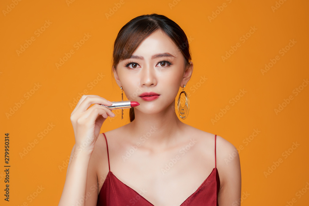 Attractive girl rouging her lips with red lipstick. Isolated on yellow background Attractive girl rouging her lips with red lipstick. Isolated on yellow background
