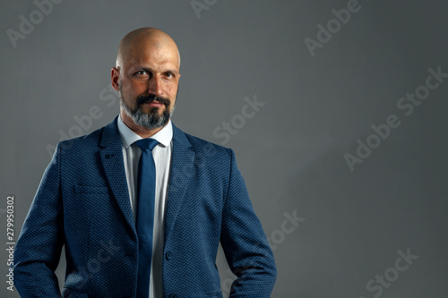 Brutal bald bearded businessman in a classic suit on a gray background with copy space