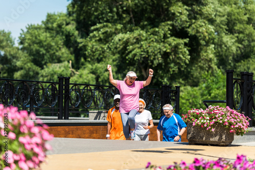 selective focus of happy retired woman celebrating triumph near multicultural pensioners in park