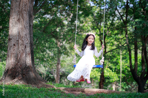 Portrait of little Asian girl playing the swing under the big tree in the nature forest select focus shallow depth of field