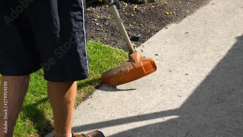 Weed wacking the edge of the grass beside the sidewalk. photo