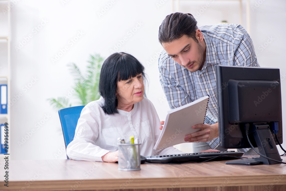 Young male employee explaining to old female colleague how to us Young male employee explaining to old female colleague how to us