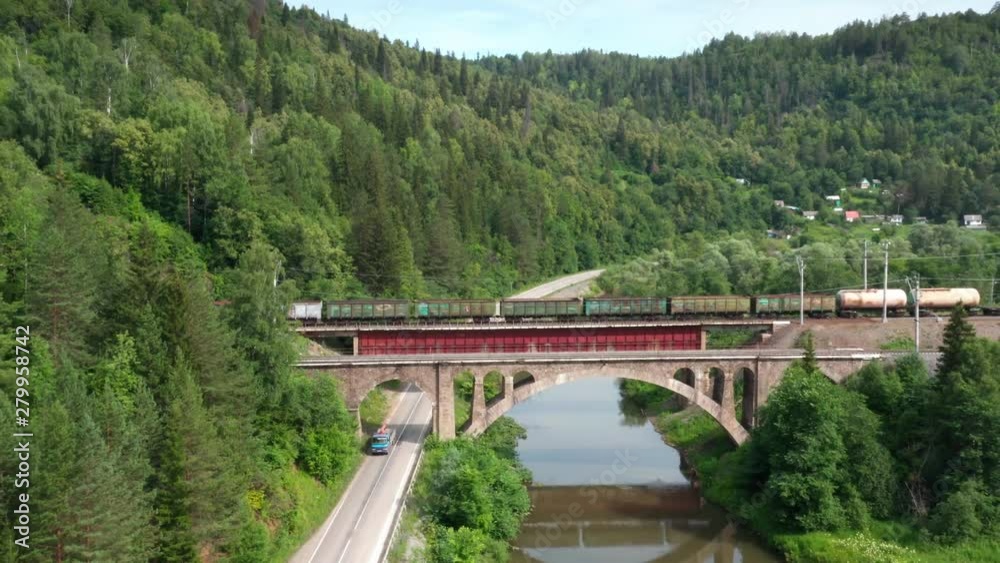 Bridge train.Pull away over the river and filming the train on the bridge in the mountains.Long train passing the bridge.Small truck driving on the road under the bridge.Pine forest on the mountains. Bridge train.Pull away over the river and filming the train on the bridge in the mountains.Long train passing the bridge.Small truck driving on the road under the bridge.Pine forest on the mountains.