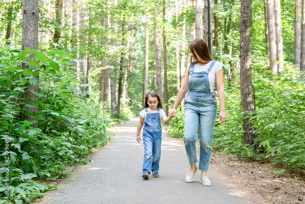 Family, summer and nature concept - Attractive young woman and beautiful little daughter girl walking in green park Family, summer and nature concept - Attractive young woman and beautiful little daughter girl walking in green park