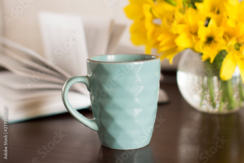 Fototapeta Naklejka Na Ścianę i Meble -  blue coffee mug, yellow flowers in transparent bowl and a book on a wooden table