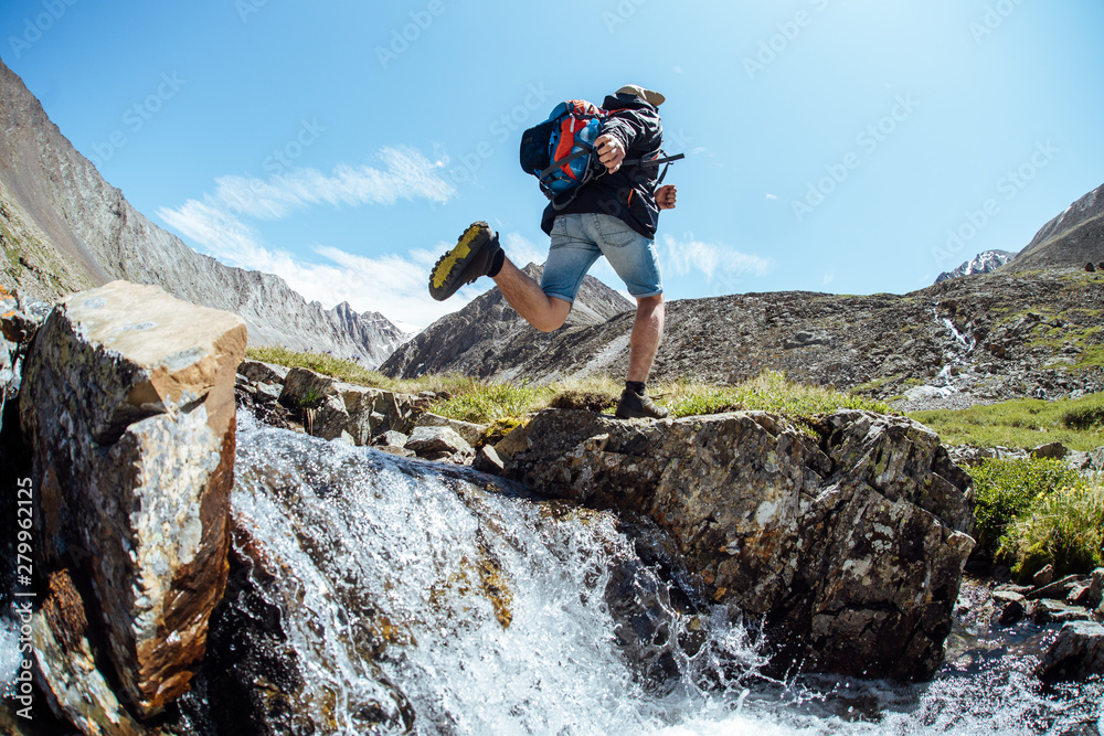 Man tourist jumps from a big rock in the mountains across the river