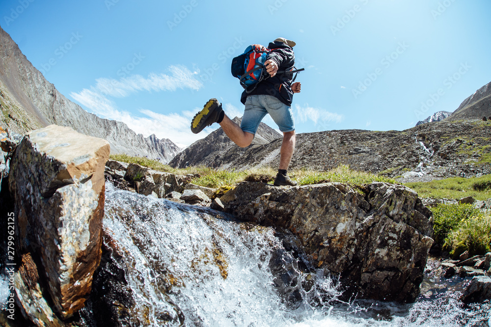 Man tourist jumps from a big rock in the mountains across the river Man tourist jumps from a big rock in the mountains across the river