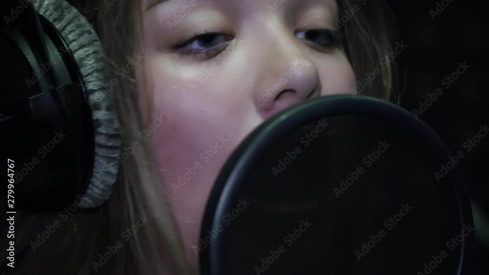 Young woman singer singing into a microphone. Vocal recording studio. Young woman singer singing into a microphone. Vocal recording studio.