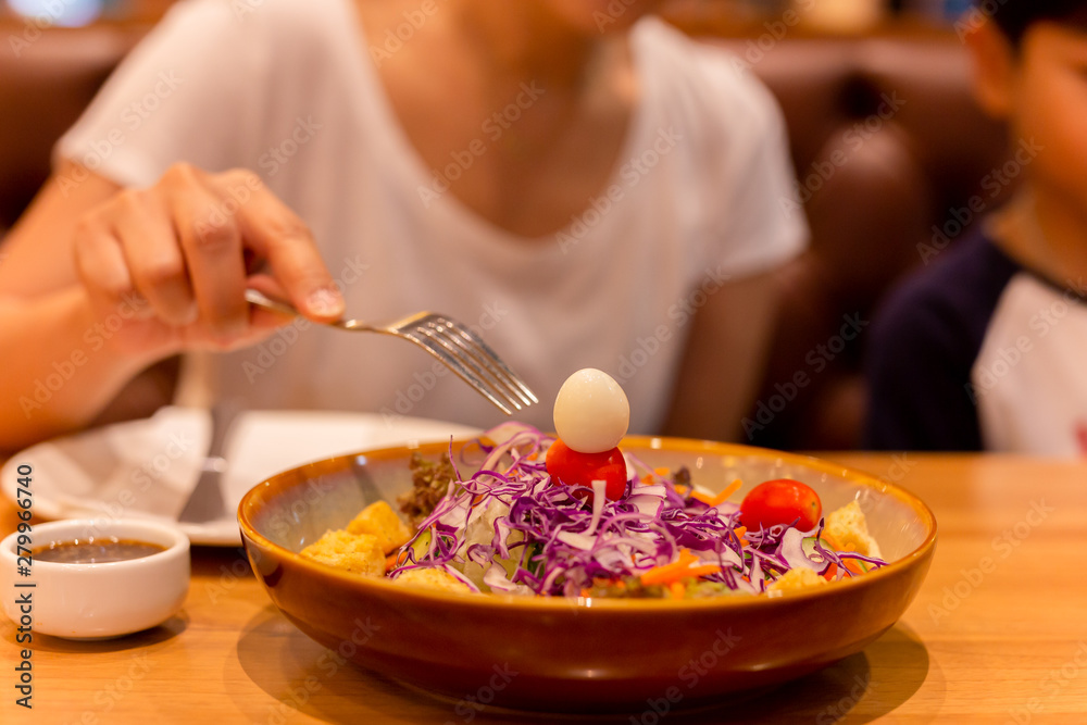 Woman hand with fork eating salad with tomato and quail egg in a plate. Woman hand with fork eating salad with tomato and quail egg in a plate.