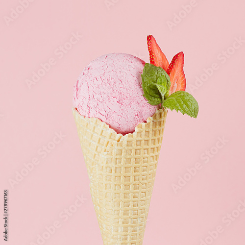Pink creamy ice cream scoop in crisp waffle cone with strawberry slices, mint leaf on pink wall, square, closeup, top.