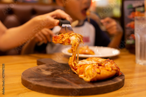 Hand taking slice pizza from wooden tray with young boy eating in background,