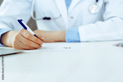 Female doctor filling up prescription form while sitting at the desk in hospital closeup. Healthcare, insurance and excellent service in medicine concept