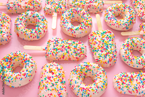 festive background of popsicles and donuts with sprinkles and icing over pink background, close up