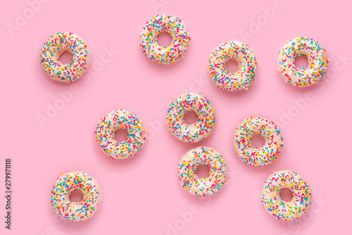 donuts with sprinkles and icing over pink background, close up
