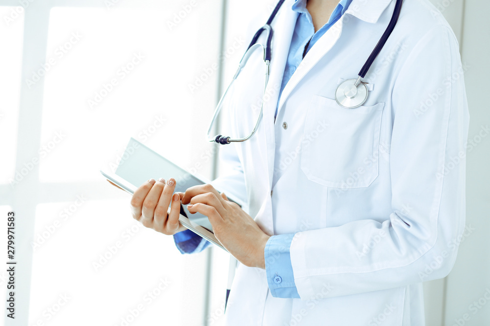 Woman doctor using tablet computer while standing straight in hospital closeup. Healthcare, insurance and medicine concept Woman doctor using tablet computer while standing straight in hospital closeup. Healthcare, insurance and medicine concept