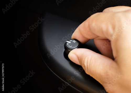 The driver's hand adjusts the wing mirror direction control switch in the car.