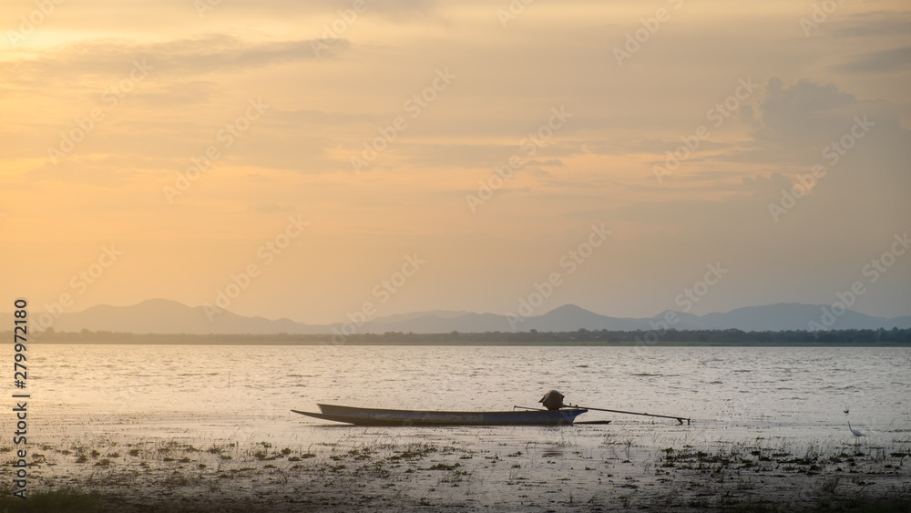 Naklejka premium lonely fishing boat docked in calm lake. wooden fishing boat in a still lake water. image of wooden fishing boat moored on the shore
