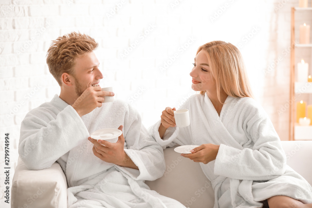 Happy young couple in bathrobes drinking coffee at home