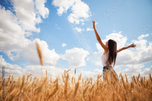 Happy woman enjoying the life in the field. Nature beauty, blue sky,white clouds and field with golden wheat. Outdoor lifestyle. Freedom concept. Woman jump in summer field