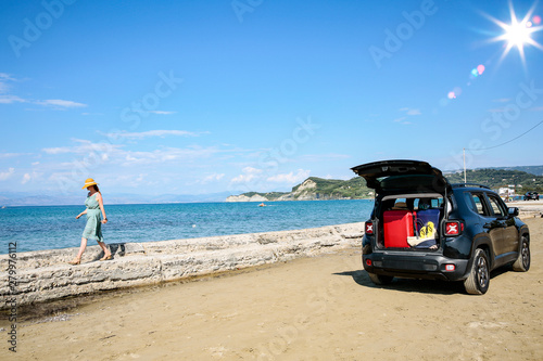 A woman in a hat and sunglasses and a car on a sunny sandy beach © magdal3na