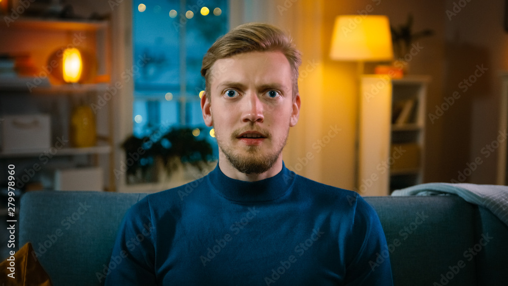 Portrait of a Handsome Man Sitting on a Couch at Home at Night, Watching Gore Horror Movie on TV. He Gets Really Scared, Confused and Disgusted. Portrait of a Handsome Man Sitting on a Couch at Home at Night, Watching Gore Horror Movie on TV. He Gets Really Scared, Confused and Disgusted.