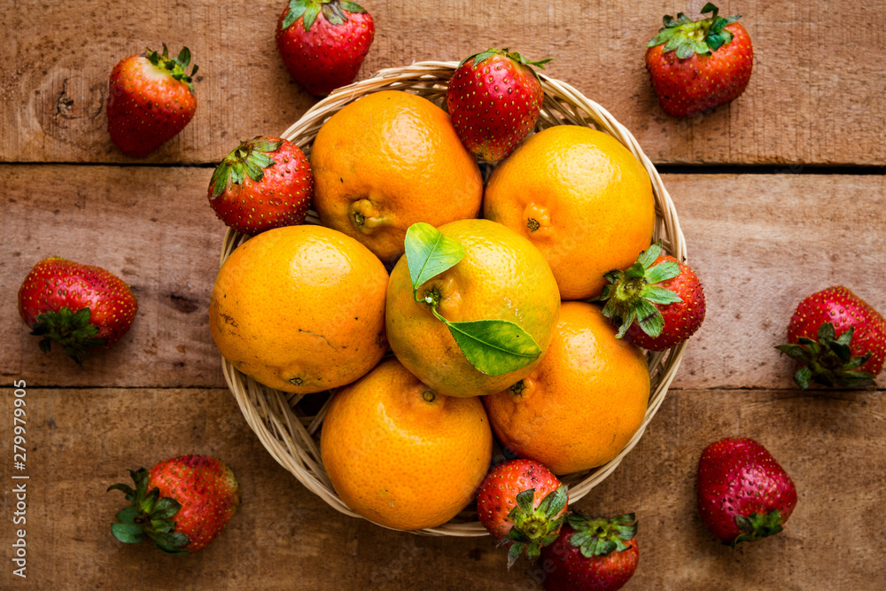 Fresh organic oranges and strawberries on wooden table - flat lay healthy food concept image with copy space for text.