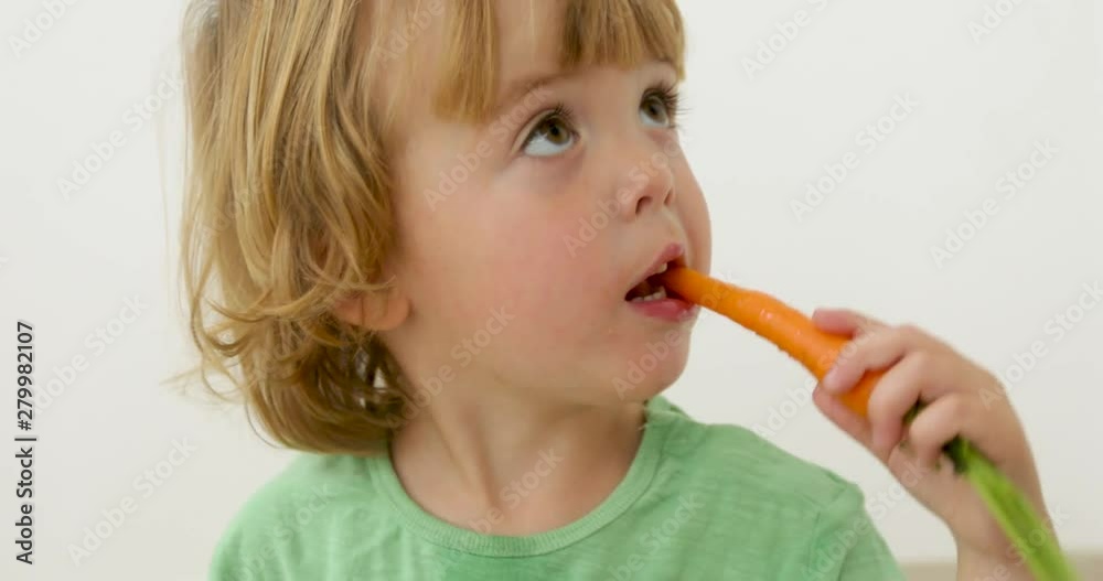 Three years old child boy bites carrot on white background Three years old child boy bites carrot on white background