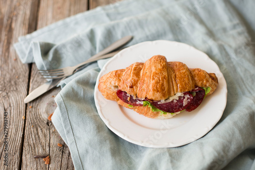 Croissant sandwich on the wooden table with salami, cheese and fresh salad food photography