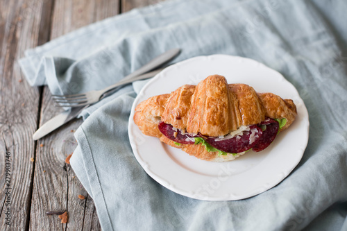 Croissant sandwich on the wooden table with salami, cheese and fresh salad food photography