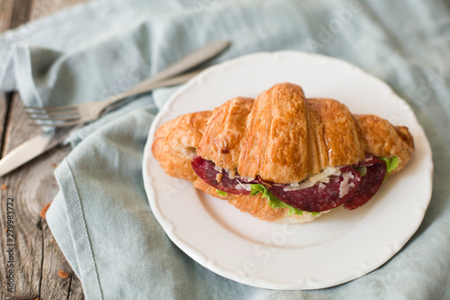 Croissant sandwich on the wooden table with salami, cheese and fresh salad food photography
