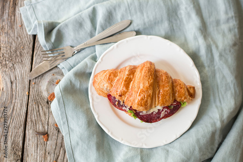 Croissant sandwich on the wooden table with salami, cheese and fresh salad food photography