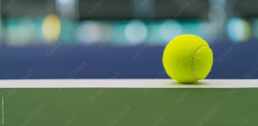 one new tennis ball on white line in blue and green hard court with beautiful bokeh, copy space on left