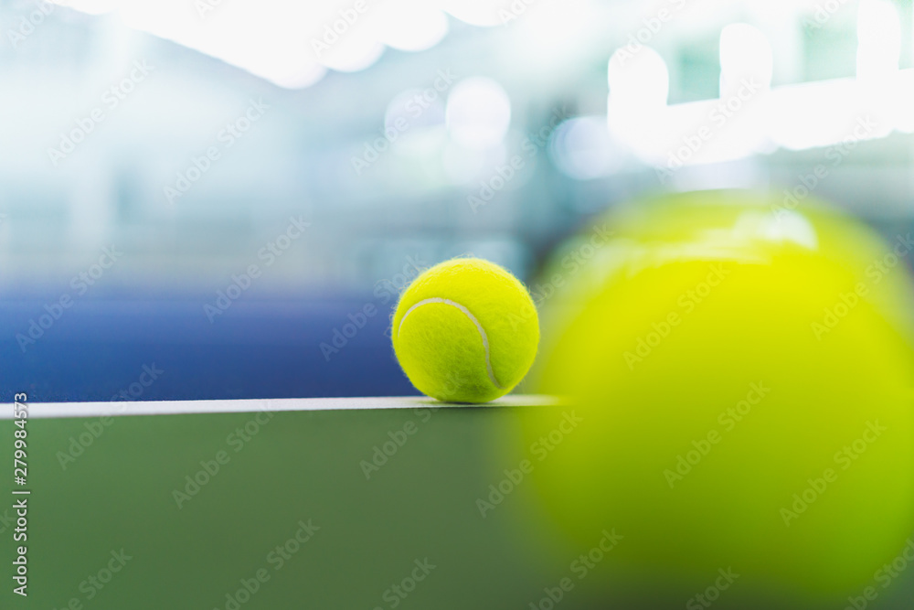 one new tennis ball on white line in blue and green hard court with blurred ball on right foreground